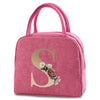 A pink insulated canvas lunch bag featuring a large gold letter S decorated with small flowers.