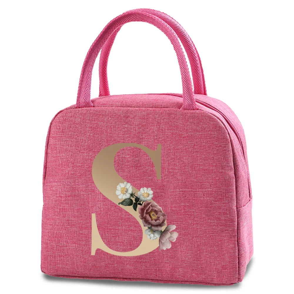 A pink insulated canvas lunch bag featuring a large gold letter S decorated with small flowers.