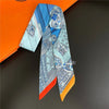 A blue and white patterned silky twill ribbon scarf displayed against an orange box.