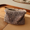 Pochette de rangement cosmétique en tissu gris plié avec de petits pois noirs et dorés sur une surface en bois.