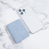 A white smartphone and a light blue card wallet are displayed on a marble surface.