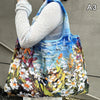A woman holds a large, colorful floral print nylon shopping tote bag against a gray wall.