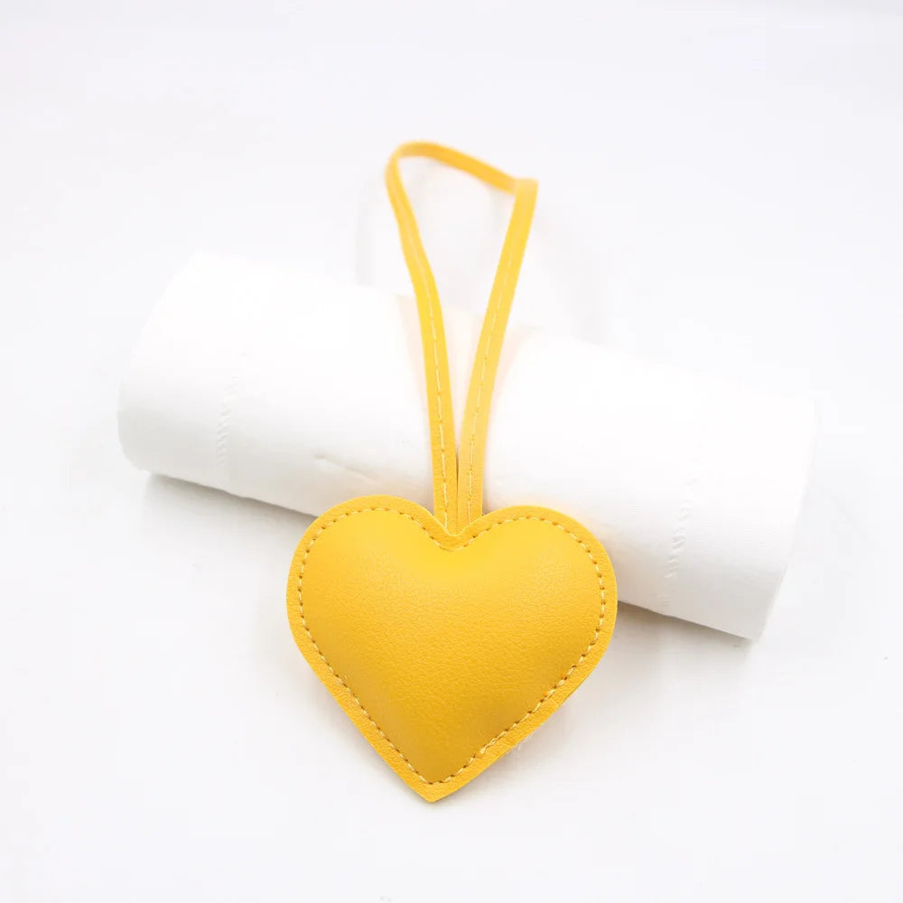 A yellow PU leather heart-shaped keychain with a thin yellow loop attached to a white cylindrical object.