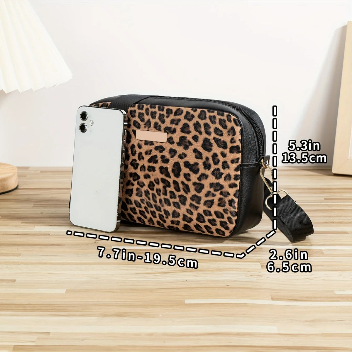 A black leopard print crossbody bag next to a white smartphone, showing its dimensions.
