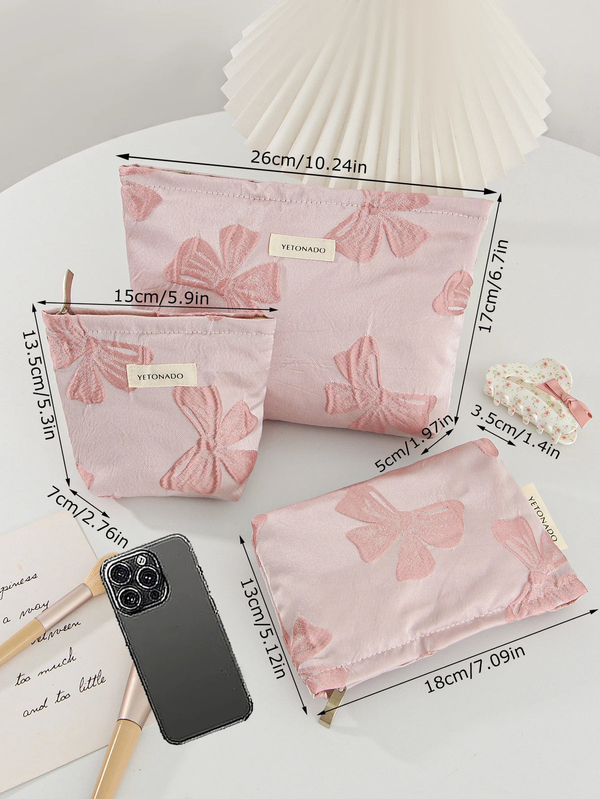 Pink bow knot cosmetic organizer bags displayed next to a smartphone and cosmetic tools.