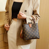 A woman wearing a beige blazer and light pants holds a dark brown Western floral bucket bag.