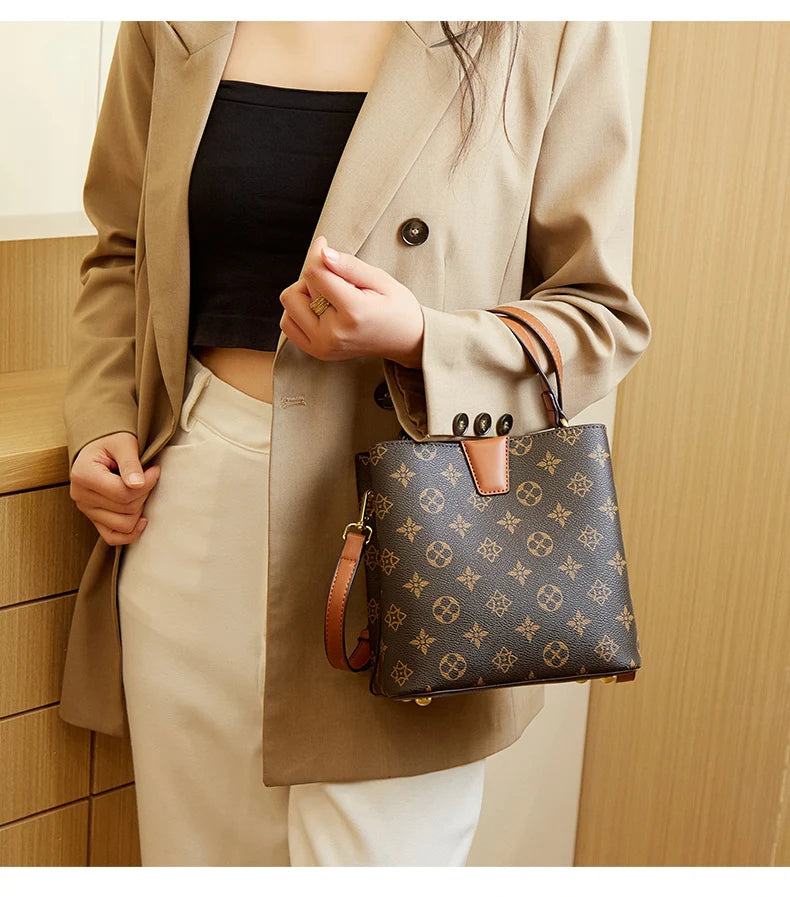 A woman wearing a beige blazer and light pants holds a dark brown Western floral bucket bag.