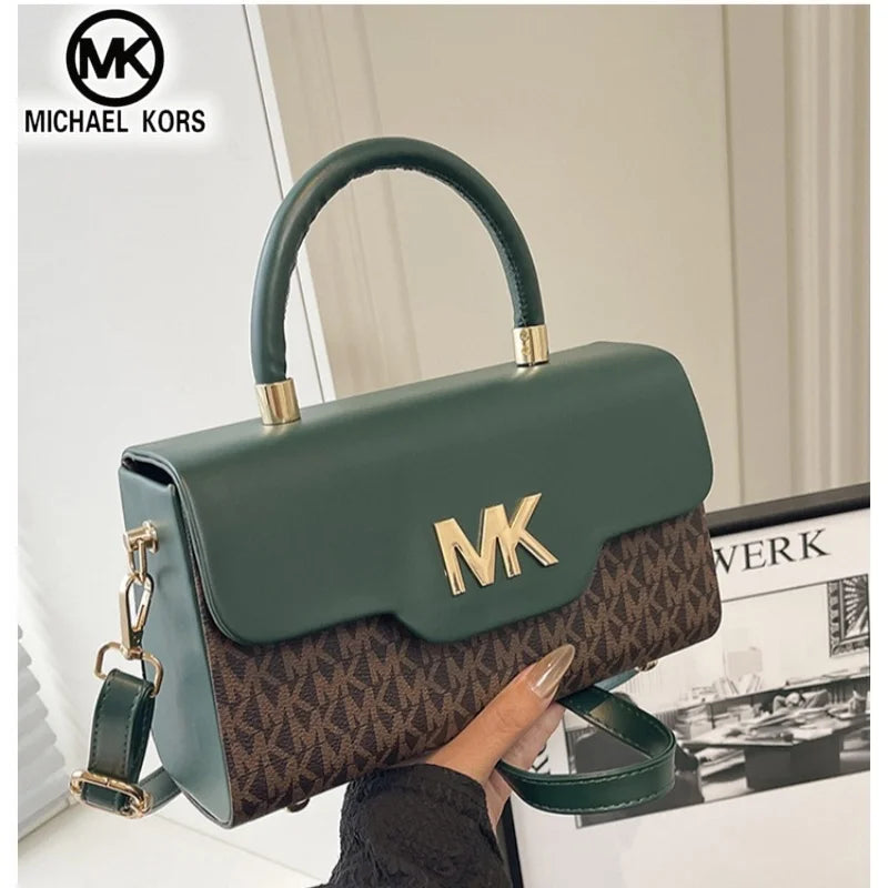 A dark green Michael Kors letter square crossbody bag with gold hardware being held by a person.