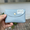 A hand holds a light blue genuine leather card holder with a gold-colored clasp and a white tag.