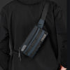 A person wearing a black hoodie holds a dark gray multifunctional chest bag against their torso.