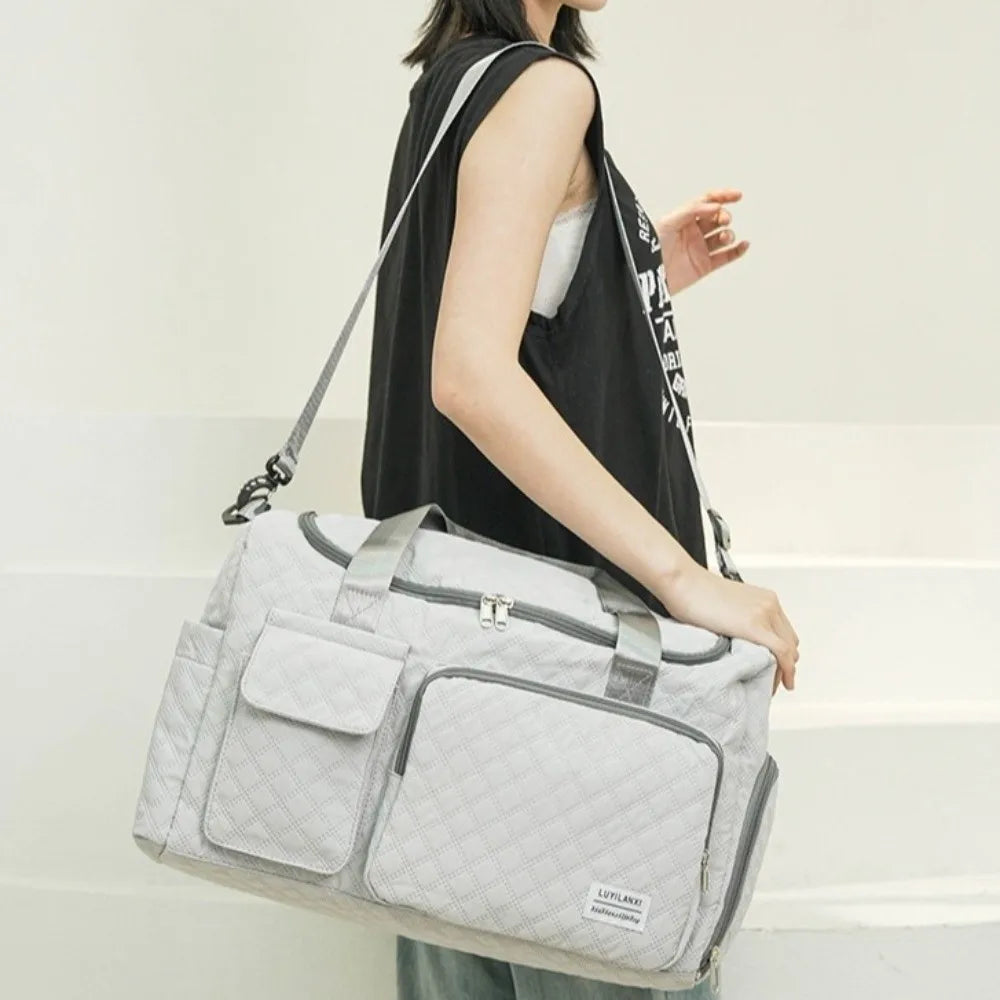 A woman is carrying a light gray quilted portable travel duffle bag with black straps.