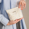 A hand holds a cream-colored floral canvas makeup bag with the text DIDF BAG against a light blue shirt.