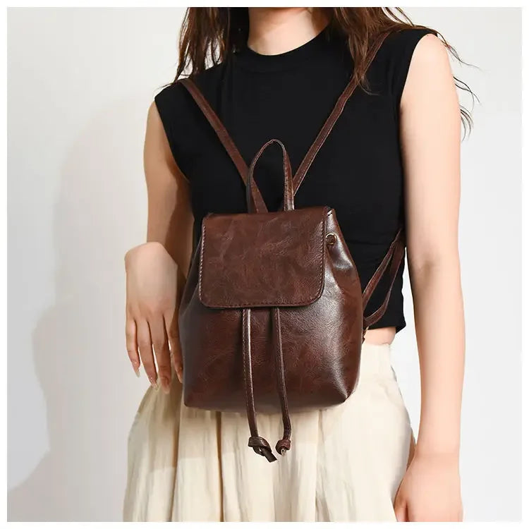 Une femme portant un haut noir et un pantalon clair tient un mini sac à dos à cordon marron rétro.