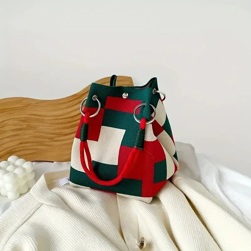 A retro knitted bucket handbag in red and green plaid fabric resting on a white garment.