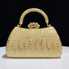 A gold crystal-embellished evening clutch bag with a chain strap resting on a white surface.