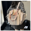 A woman is holding a beige nylon shoulder bag with striped leather straps in a casual indoor setting.