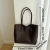 A dark brown leather tote bag hanging against a white wall with a measurement scale.