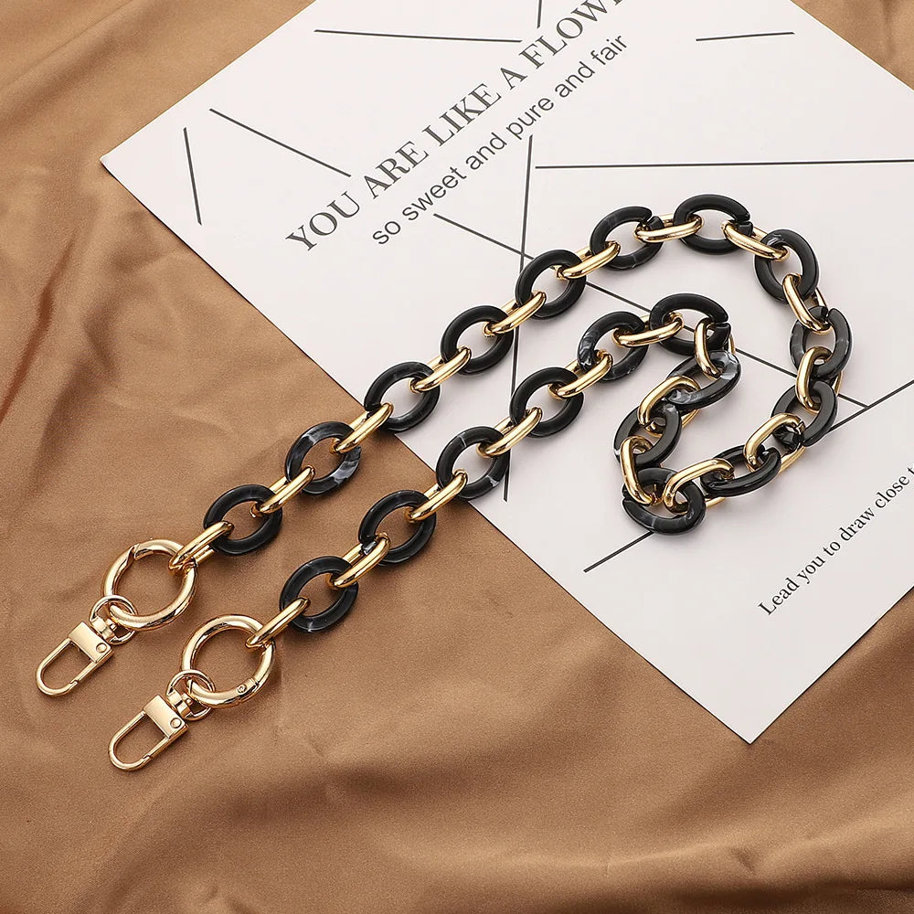 A gold and black acrylic handbag strap chain laid on a brown paper with text.