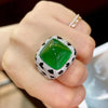 A hand is holding a luxury leopard crystal statement ring featuring a vibrant green faceted gemstone and a silver pave settin