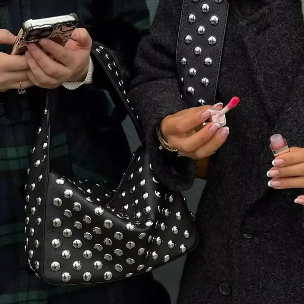A person holds a black designer metal rivet shoulder bag and a red nail polish bottle.