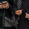 A close-up of a black luxury metal rivet shoulder bag being held by a person.