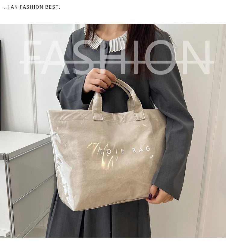 A woman holds a clear waterproof PVC tote bag with gold lettering against a light background.