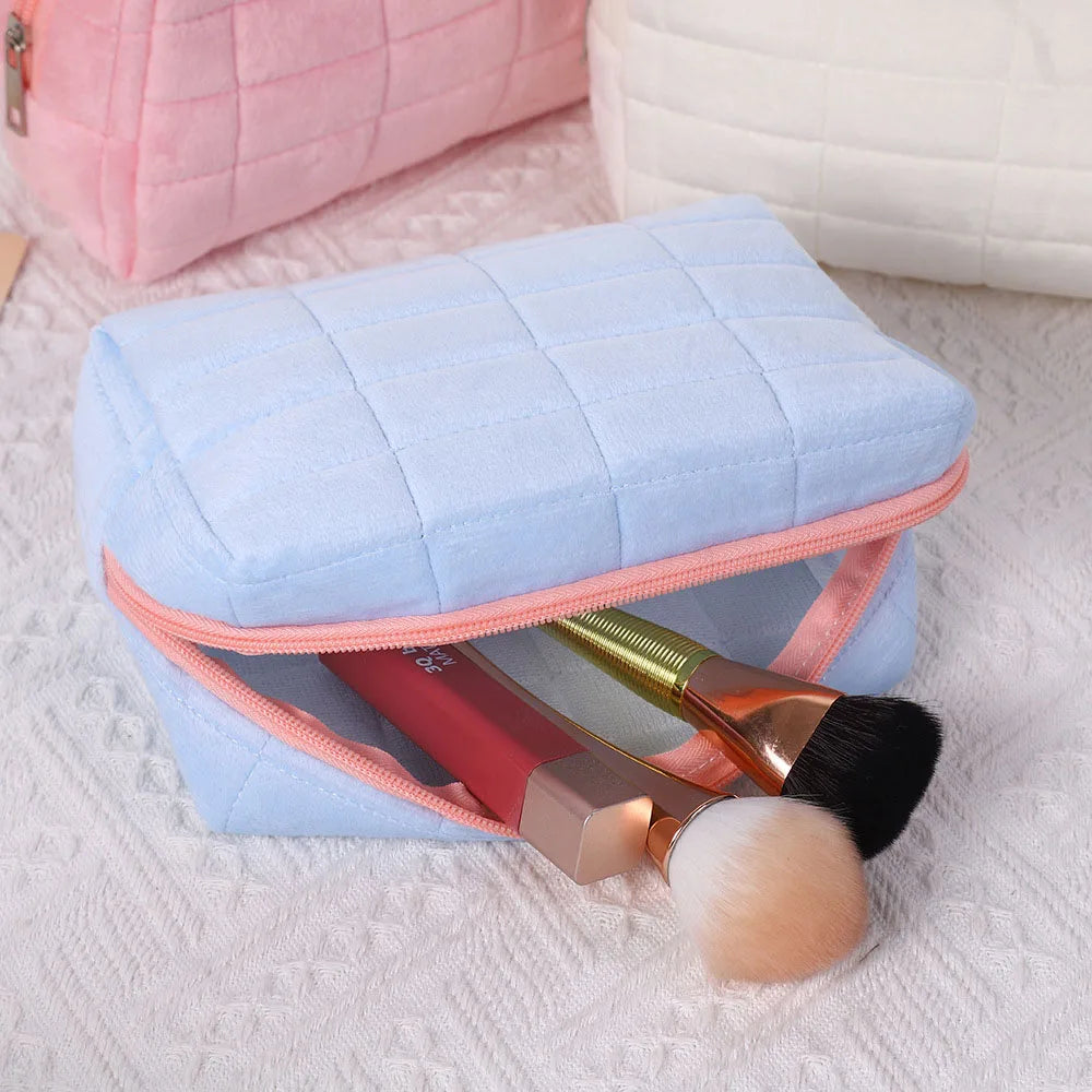 Light blue quilted velvet cosmetic and toiletry bag with a pink lining and a gold makeup brush inside