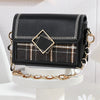 Pochette noire ajustable avec rallonges de chaîne dorées et surpiqûres décoratives sur un présentoir blanc.