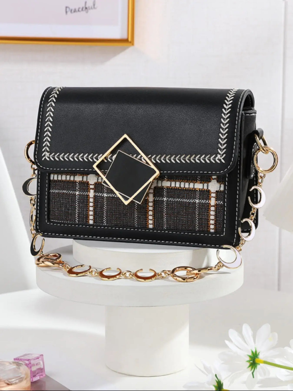 Pochette noire ajustable avec rallonges de chaîne dorées et surpiqûres décoratives sur un présentoir blanc.