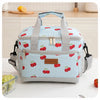 A light blue insulated thermal lunch bag with a patterned fabric and gray straps is shown on a white table.
