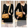 A woman models a tan leather shoulder strap attached to a small beige leather bag.