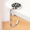A round silver metal bag hanger with a black and white cow print insert is displayed on a white surface.