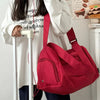 A person is holding a red canvas crossbody travel tote bag with white and black text on a white shirt.