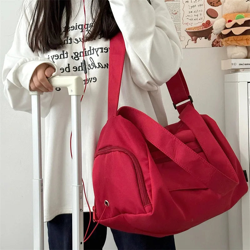 A person is holding a red canvas crossbody travel tote bag with white and black text on a white shirt.