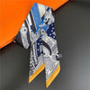 A silky twill ribbon scarf featuring a pattern of blue, white, and black geometric designs displayed against an orange backgr