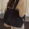 A woman is holding a black corduroy shoulder bag with a zipper against a light background.