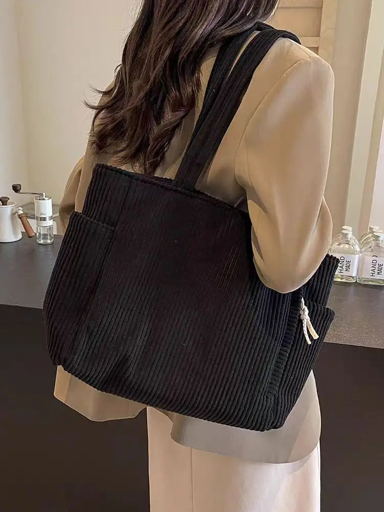 A woman is holding a black corduroy shoulder bag with a zipper against a light background.