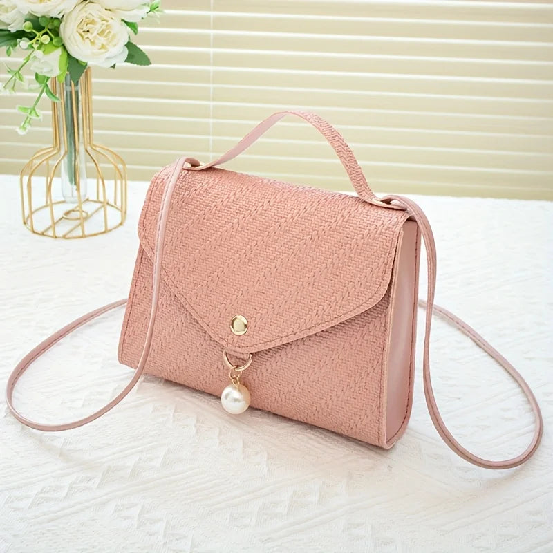 A light pink beaded square crossbody bag with a gold-tone charm rests on a white surface.