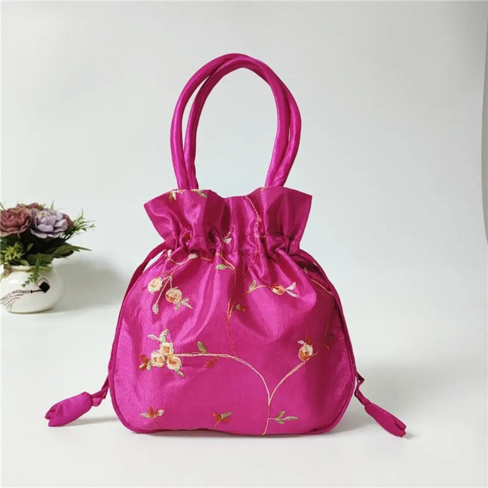 Clutch de fiesta rosa brillante con lazo de purpurina y bordado floral sobre una superficie blanca.