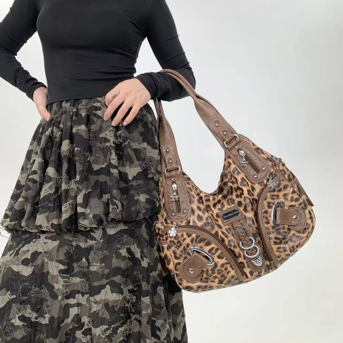 A woman wearing a black top and camouflage skirt holds a brown leopard print crossbody shoulder bag.