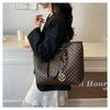 A woman holds a black faux leather letter-print tote bag with gold hardware against a light background.