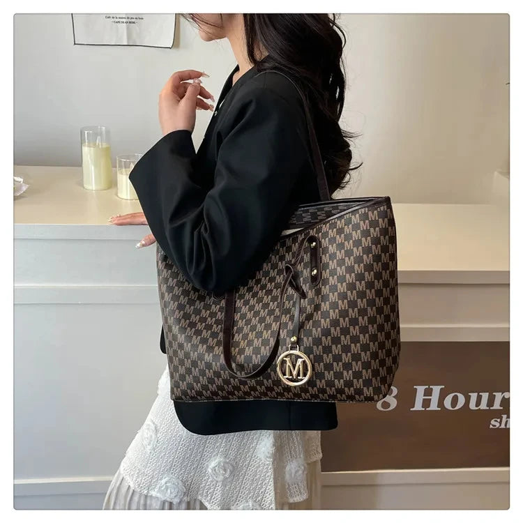 A woman holds a black faux leather letter-print tote bag with gold hardware against a light background.