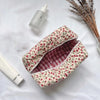 Bolsa de maquillaje con cremallera acolchada floral y forro a cuadros, junto a una pequeña botella blanca.