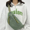 A woman wearing a light gray hoodie holds a olive green corduroy waist pack.