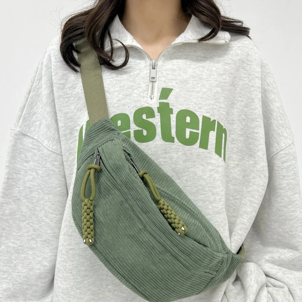 A woman wearing a light gray hoodie holds a olive green corduroy waist pack.