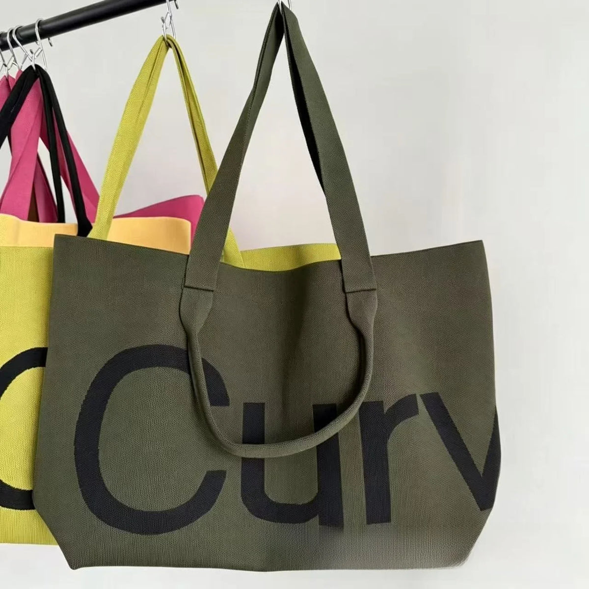 A dark olive green knitted large tote bag with a black logo on a white background.