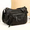 A black luxury leather tote bag with zippered compartments and hardware is shown against a light background.