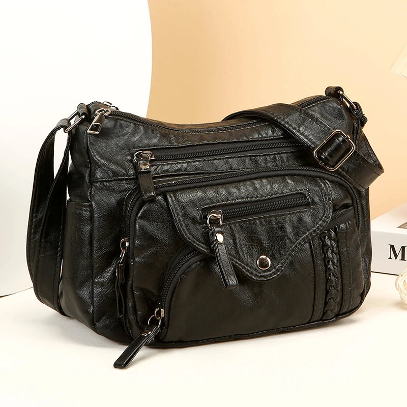 A black luxury leather tote bag with zippered compartments and hardware is shown against a light background.