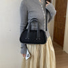 A woman wearing a grey knitted top and a cream skirt holds a black crocodile textured mini crossbody bag.