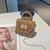 Bolso cruz floral texturizado en tono canela con correa de cadena dorada sobre una superficie blanca.